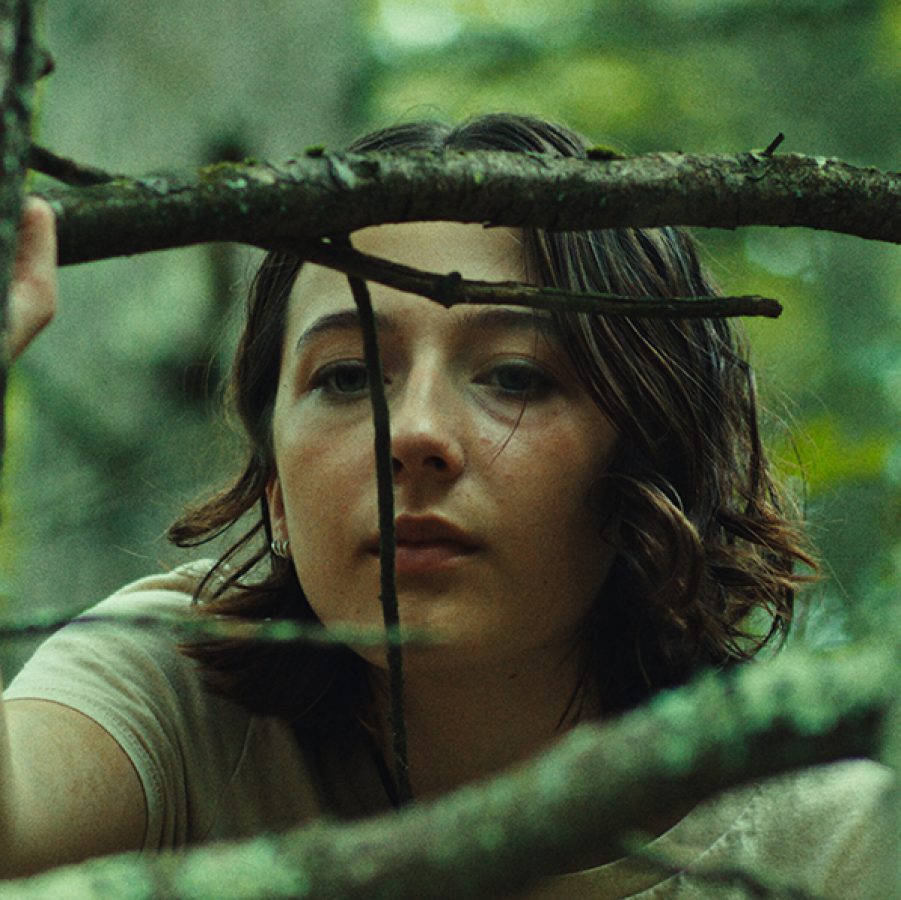 Teenager Sam (Lily Collias) peers out from among tree branches in a scene from Good One.